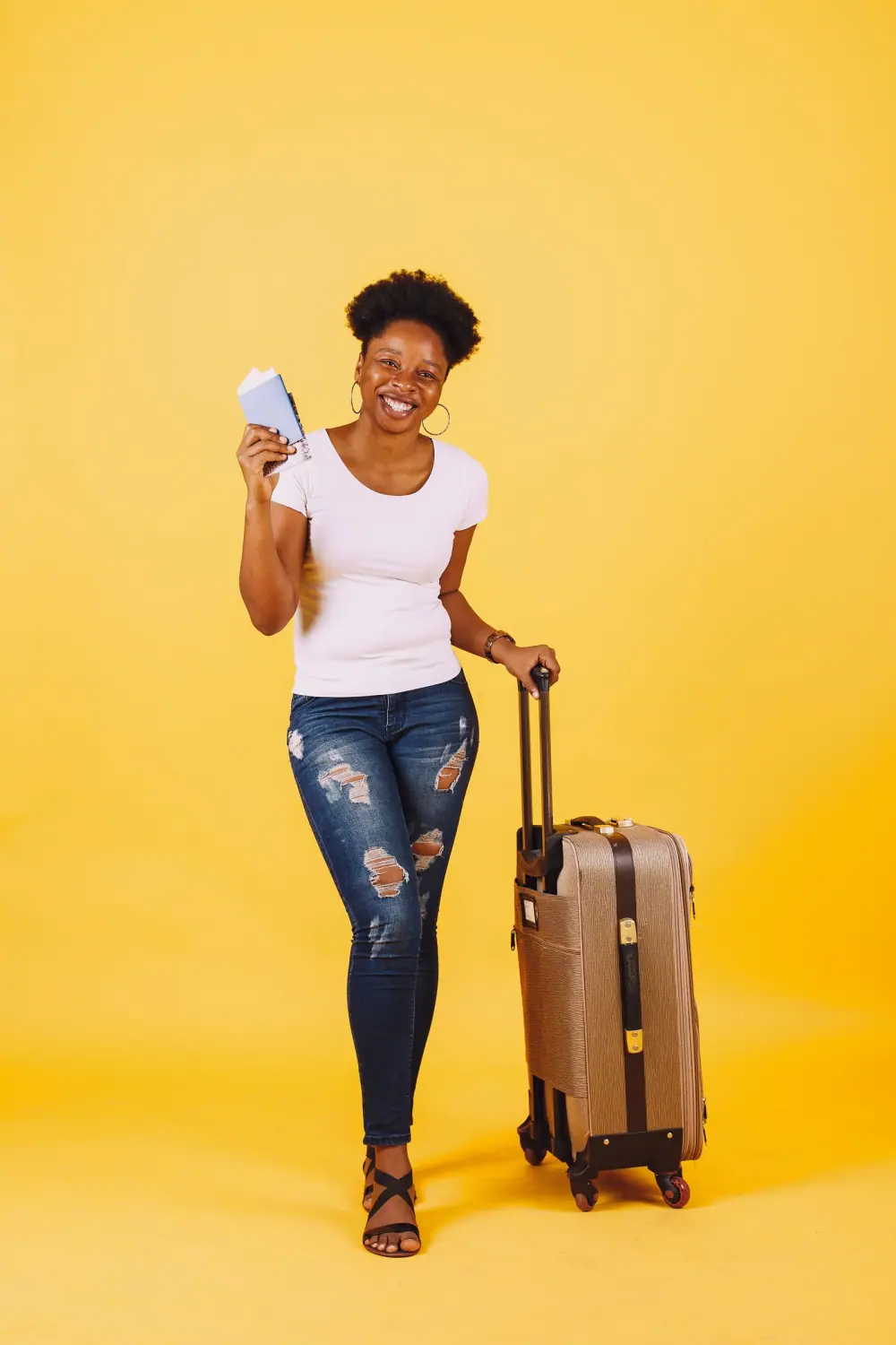 Jeune femme souriante tenant son passeport à côté de sa valise, prête à partir